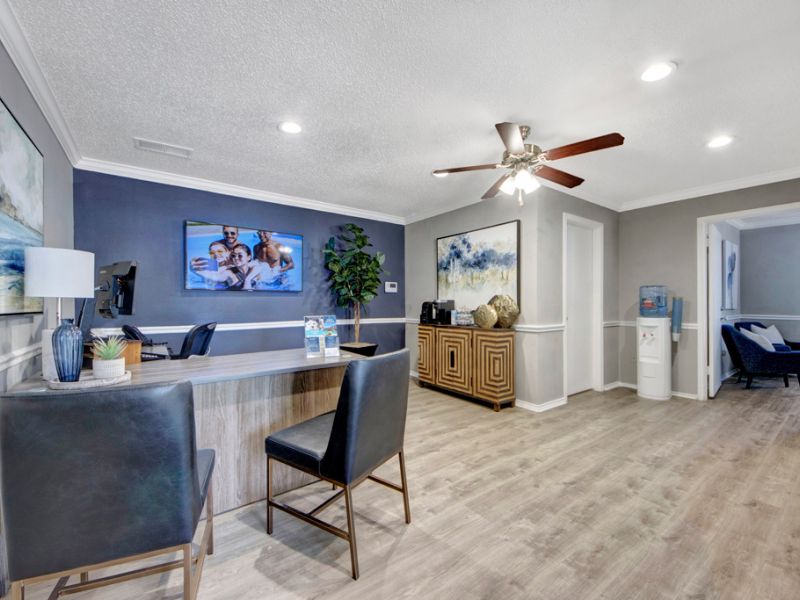 Modern office lobby with a reception desk, chairs, art on walls, a plant, and a water cooler. Light wood flooring.