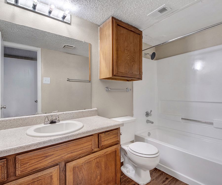 Bathroom with a wooden vanity, sink, toilet, and bathtub. Large mirror and overhead lights above the sink.