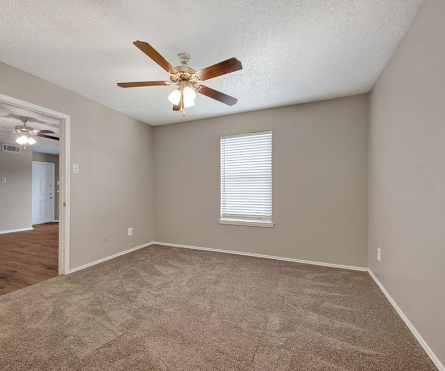 Empty room with beige carpet, beige walls, a window with blinds, and a ceiling fan with lights.