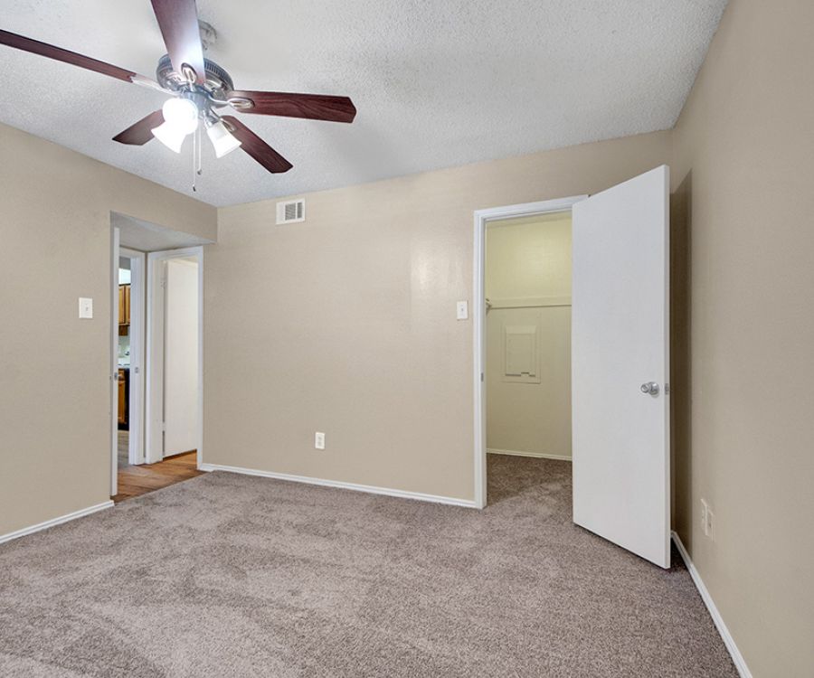 Empty room with beige walls, carpeted floor, open closet door, and ceiling fan with light.